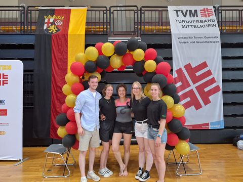 Eine Turnerin und vier Fans stehen unter einem Ballon-Bogen in Deutschlandfarben