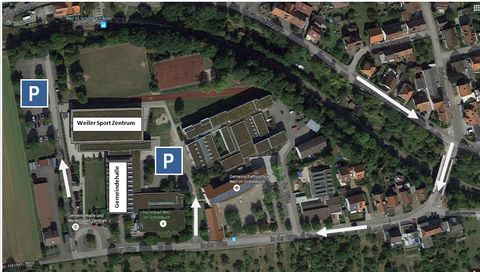 Satellitenaufnahme von Weil im Schönbuch mit eingezeichneten Markierungen. Beschriftet sind das Weiler Sport Zentrum, die Gemeindehalle, das Hallenbad Weil im Schönbuch und die Gemeinschaftsschule Weil im Schönbuch. Zwei Parkplätze sind mit blauen P-Symbolen markiert. Weiße Pfeile zeigen die Anfahrtswege über die Straße 'In der Röte'. Sichtbar sind außerdem Tennisplätze, eine Laufbahn und umliegende Wohngebäude mit Grünflächen.